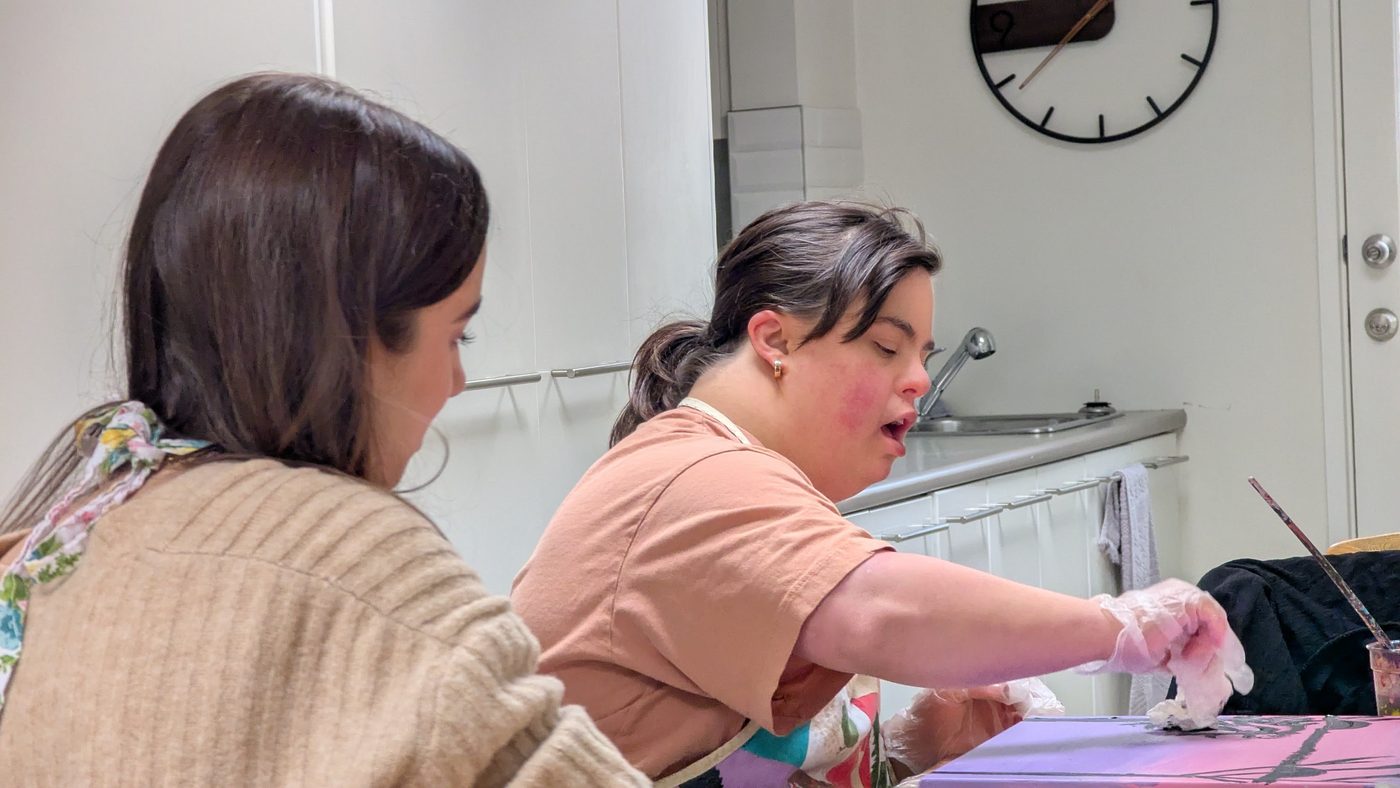 Rachel painting at a table with her Support Worker